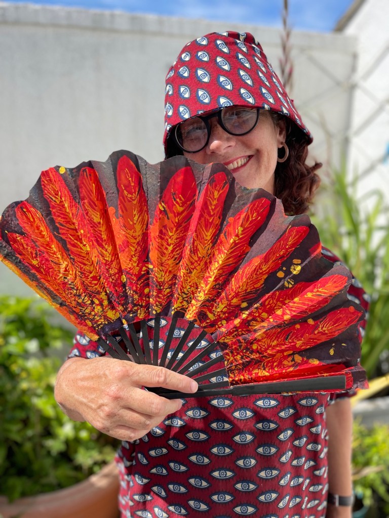 Artist Lois Blackburn holding folding fan, covered in phoenix feathers, created with batik on fabric