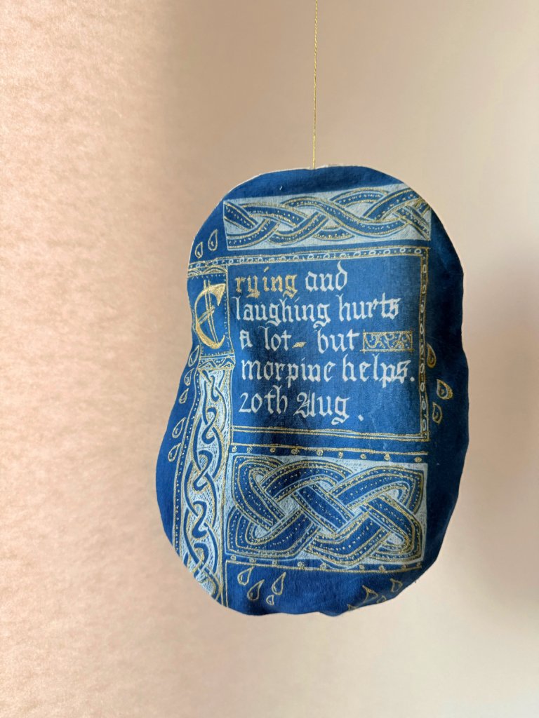 Artist Lois Blackburn's Stoma Bag Cover, illustrated with Celtic knots and words, crying and laughing.hurts, morphine helps. Cyanotype on fabric, shades of blue and gold.