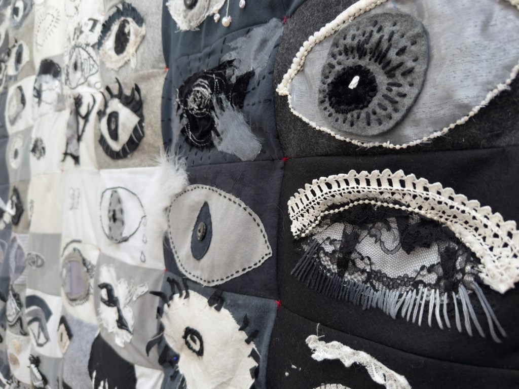 Detail of the art quilt I SEE you, over 100 embroidered eyes in black and white fabric, trimmings and stitch.