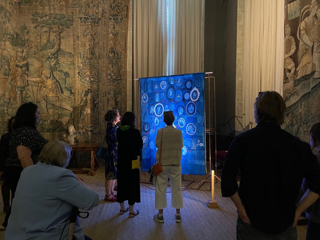 Opening event for exhibition Material Matters at Hardwick Hall. Showing audience looking at Lois Blackurn's art quilt, From Roots to the Sky.