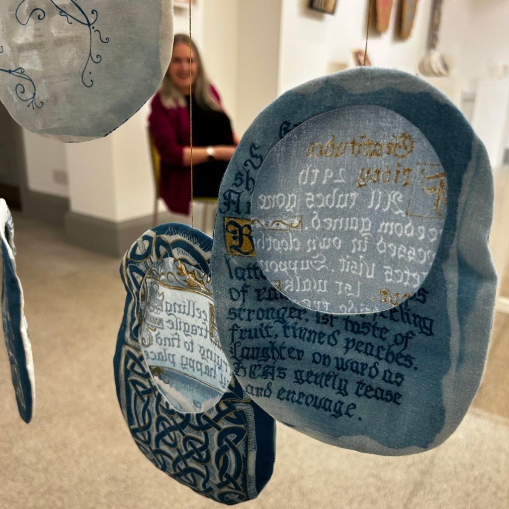 Exhibition of Stoma bag covers, cyanotype on fabric with hand calligraphy and celtic knot illustration, part of Under Repair series by Lois Blackburn.