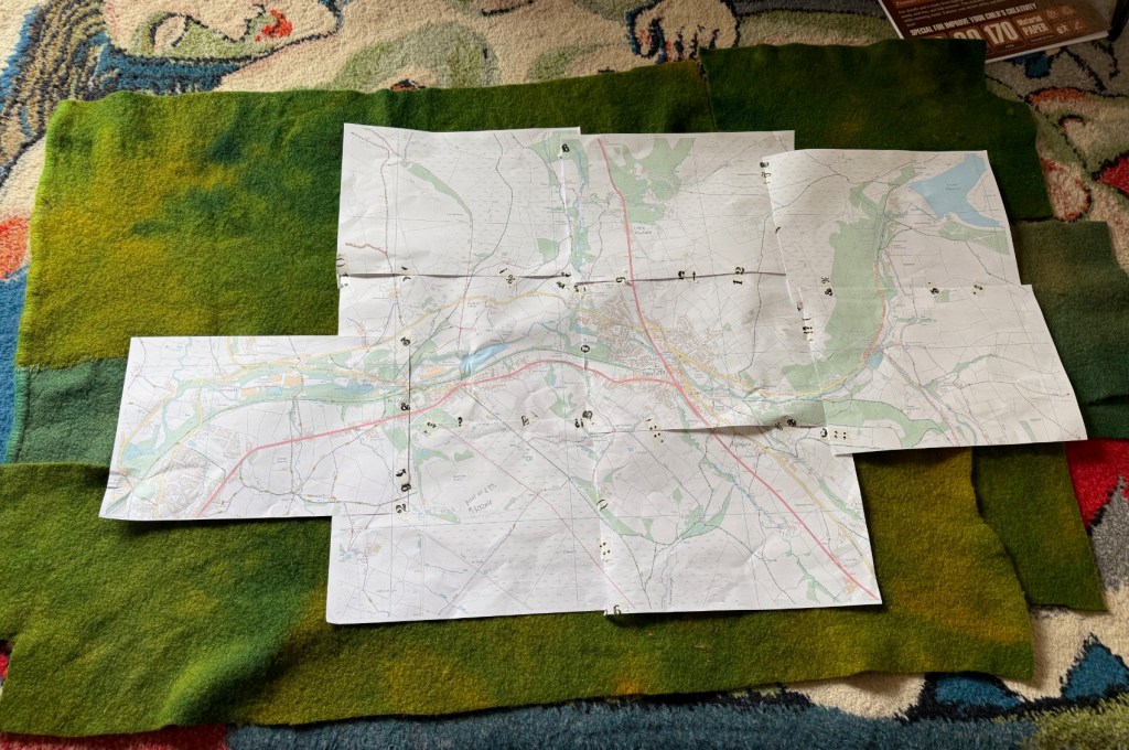 Map print outs on top of patchwork of green dyed wool blankets
