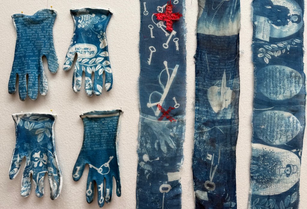 Embroidered cyanotype on fabric and gloves, sample. Part of Lost then Found series by Lois Blackburn. Picturing glasses, keys, writing,  and embroidered red crosses