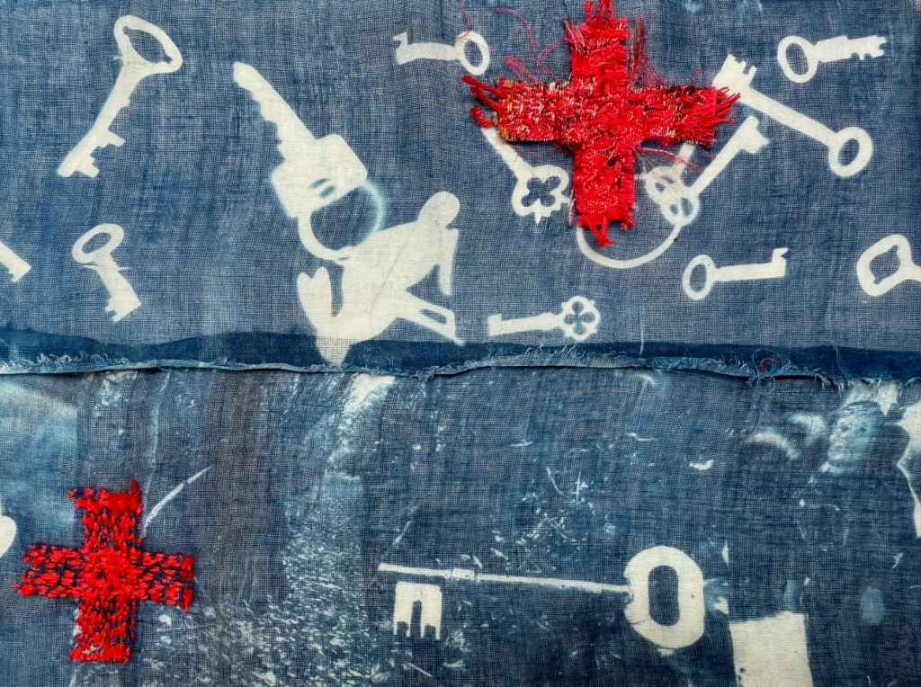 Embroidered cyanotype on fabric sample.  Part of Lost then Found series by Lois Blackburn. Picturing keys, and embroidered red crosses