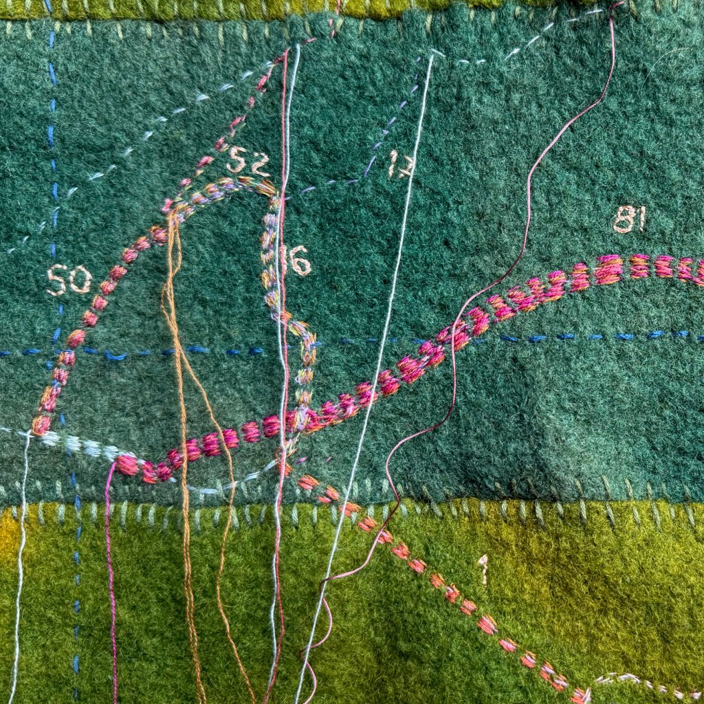 Patchwork of dyed blanket pieces, with stitched map. Threads loose as work in progress